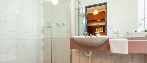 A bathroom with a glass shower enclosure, a sink with a mirror, and a towel hanging on the wall.