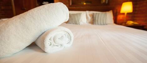 Una cama bien hecha con sábanas blancas y una toalla blanca enrollada a la izquierda.
