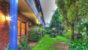 A courtyard with a brick building, a small table and chairs, and various plants.