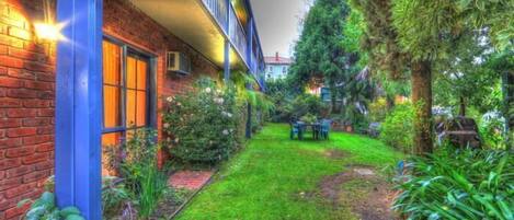 Un patio con un edificio de ladrillo, una mesa pequeña y sillas, y varias plantas.