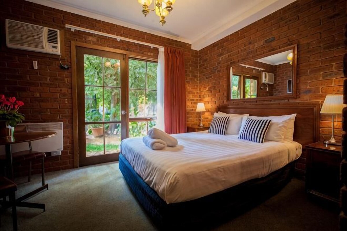 A bedroom with a brick wall, a bed, a desk, and a window.