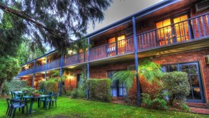 A two-story building with a balcony, surrounded by lush greenery.