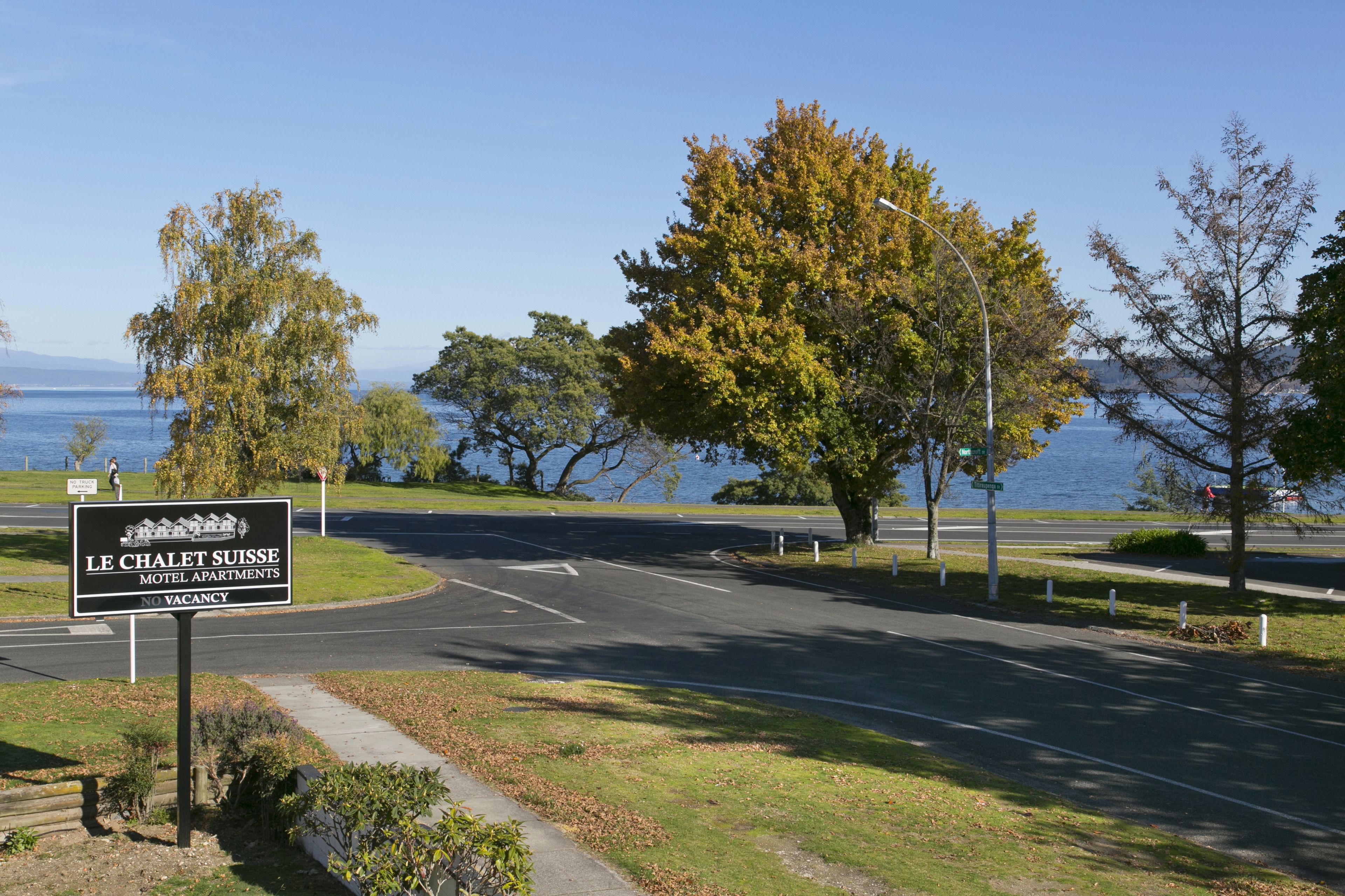 A sign for Le Chalet Suisse Motel Apartments with a view of a road and trees.