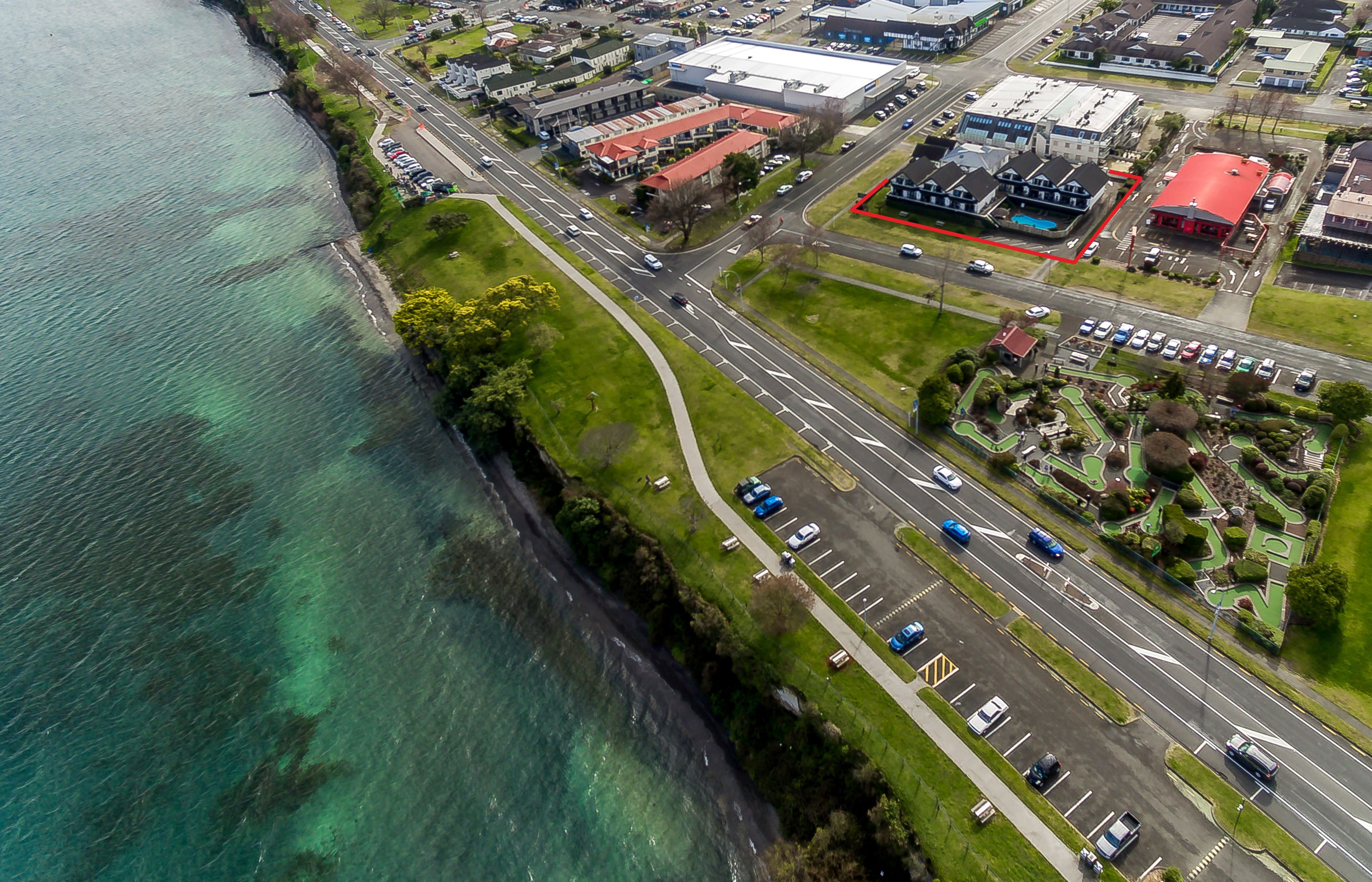 An aerial view of a coastal area with a road, buildings, and a parking lot.