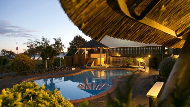 Une piscine dotée d’une terrasse en bois et d’une structure de toit en chaume.