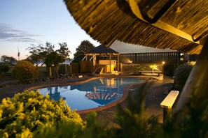 A swimming pool with a wooden deck and a thatched roof structure.