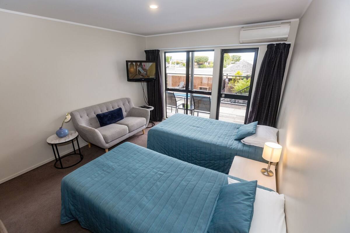 Une chambre d’hôtel avec deux lits, un canapé, une télévision et une fenêtre avec des rideaux.
