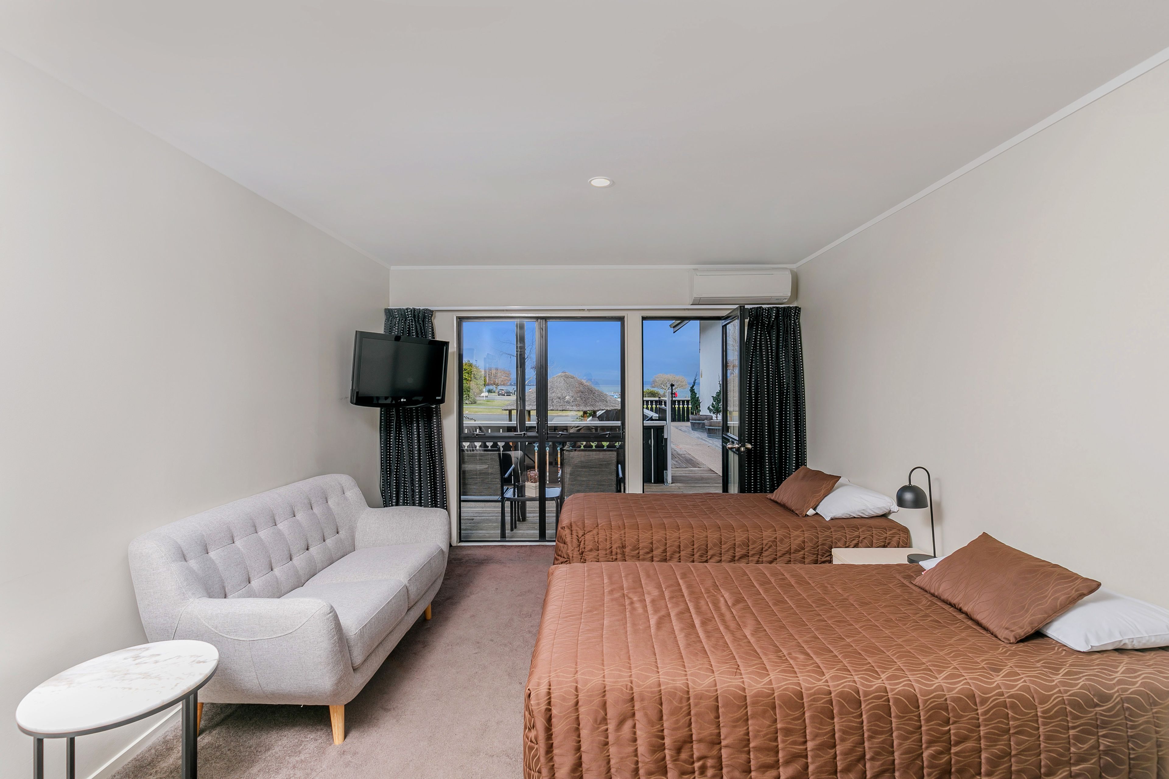 A hotel room with two beds, a sofa, a small table, a TV, and a balcony with a view.