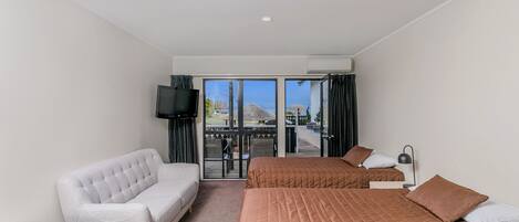 Habitación de hotel con dos camas, un sofá, una mesita, un televisor y un balcón con vistas.