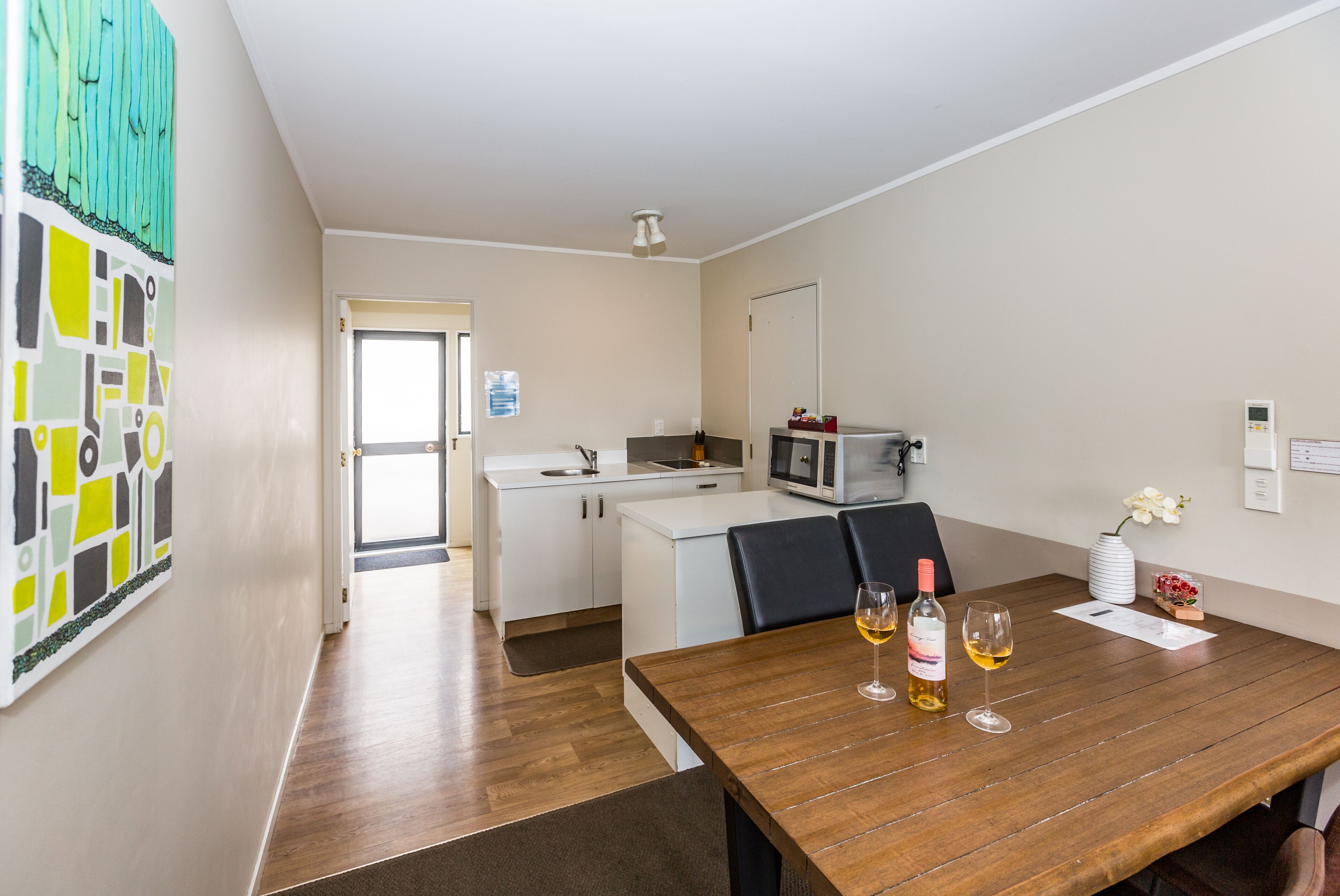 Une cuisine moderne avec des meubles blancs, un four à micro-ondes et un coin repas comprenant une table en bois dressée pour deux personnes, avec des verres à vin.
