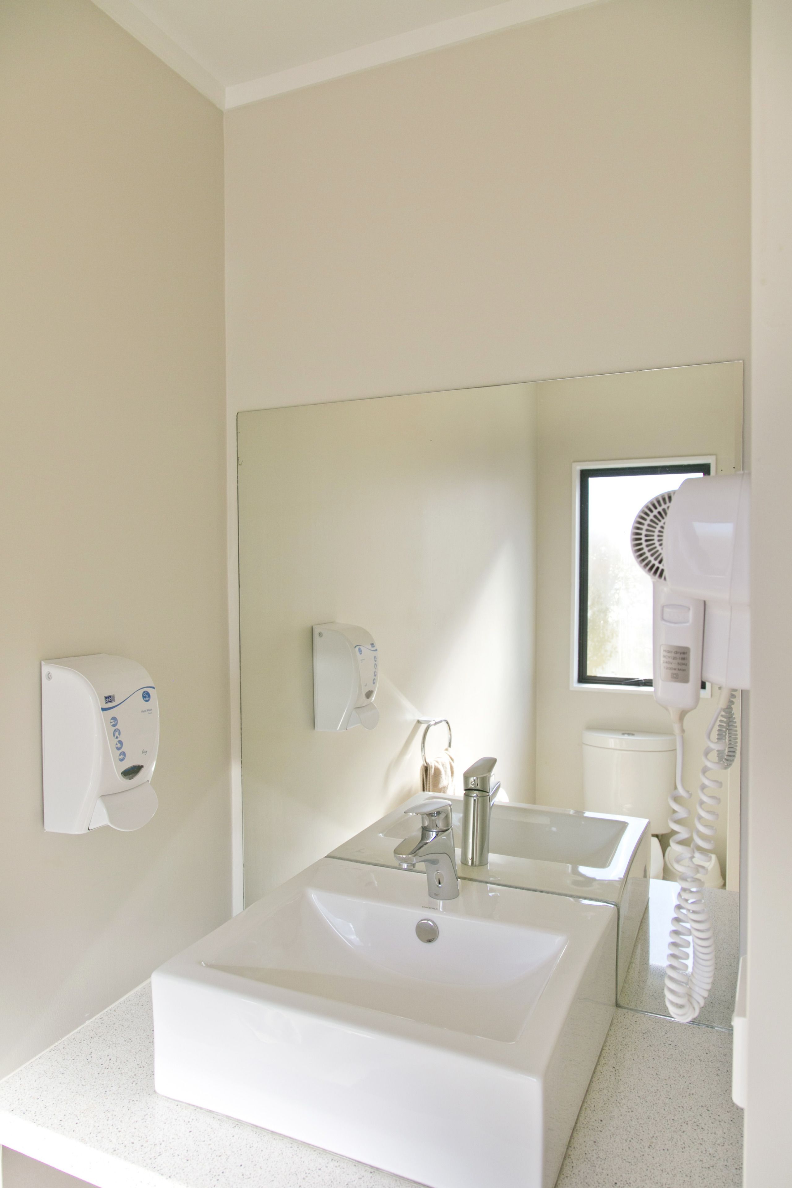 A bathroom with a white sink, a mirror, a hand dryer, and a paper towel dispenser.