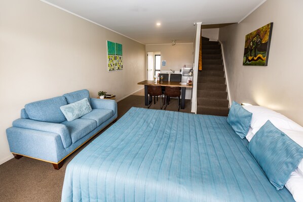 A bedroom with a large bed, a sofa, a desk, and a staircase.