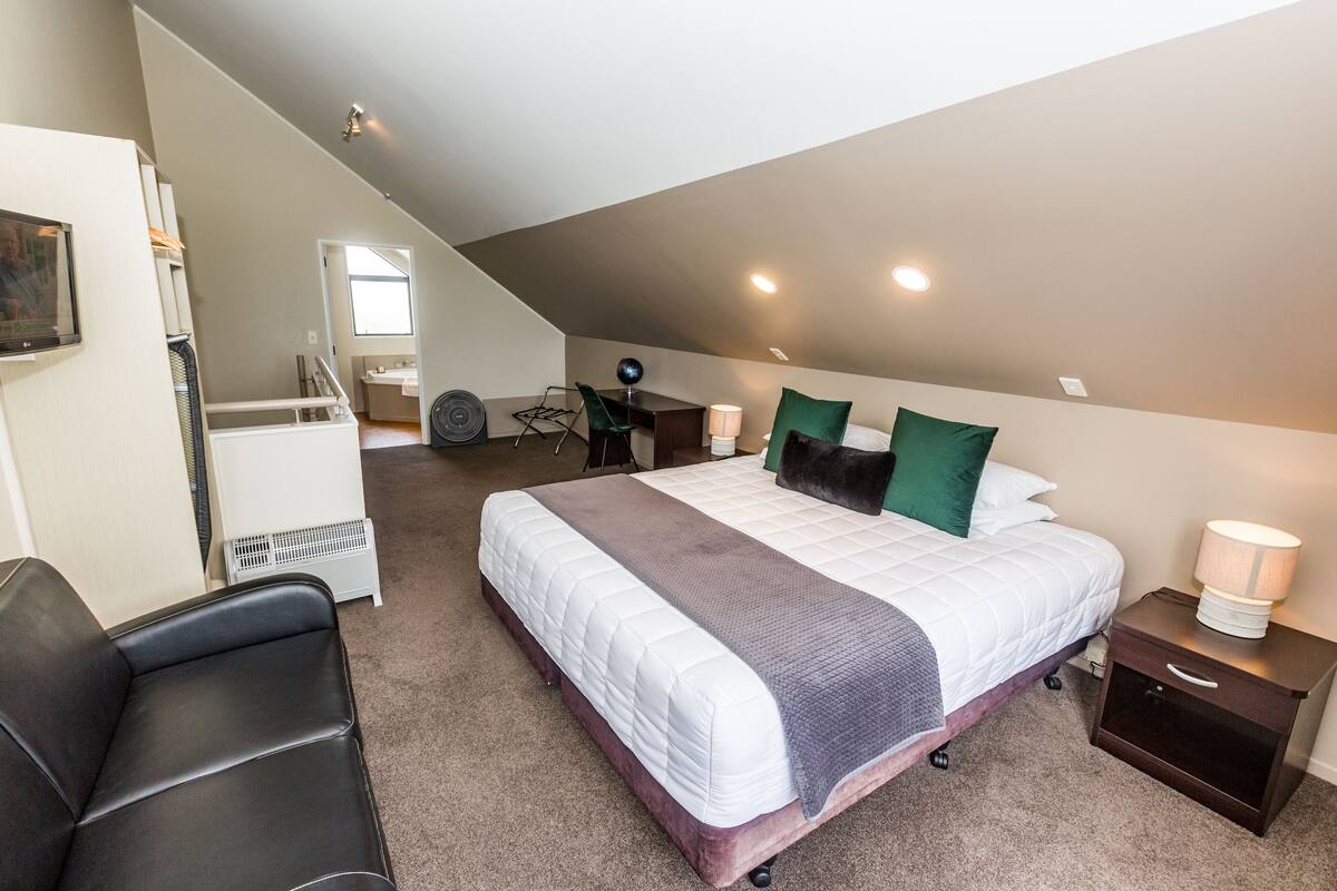 Une chambre à coucher avec un grand lit, un bureau, une chaise et une table de chevet avec une lampe.