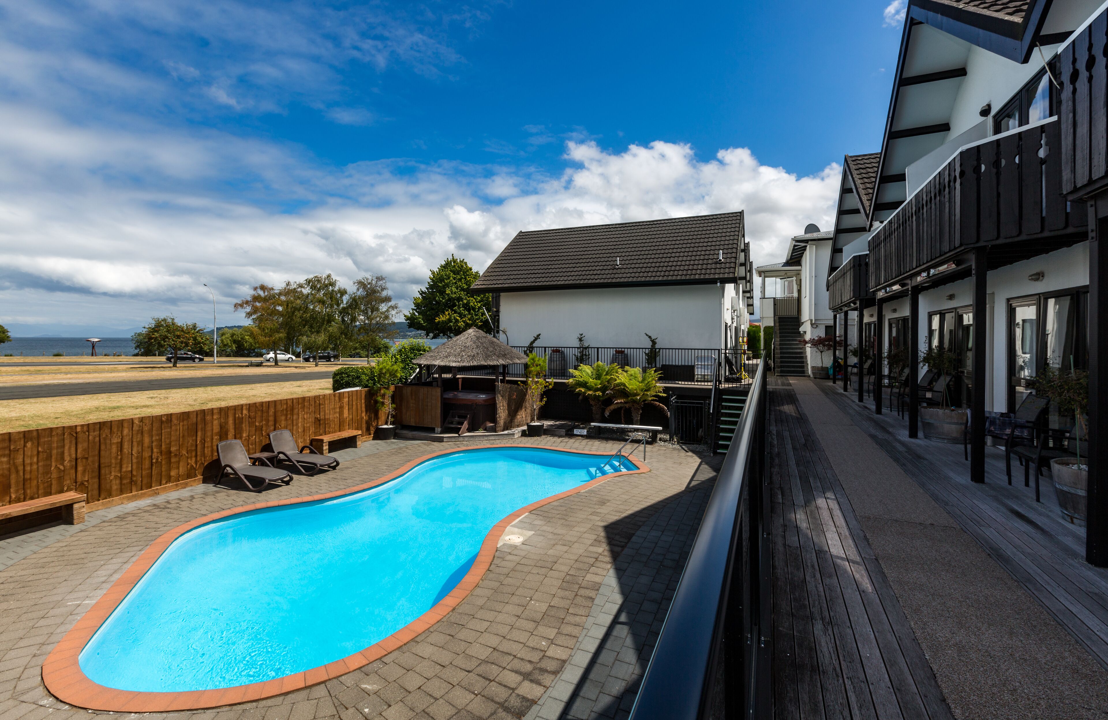 Una piscina con sillas de descanso, una terraza de madera y vista al mar.