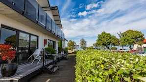 Un bâtiment moderne doté de grandes fenêtres, d’une terrasse en bois et d’un jardin bien entretenu.