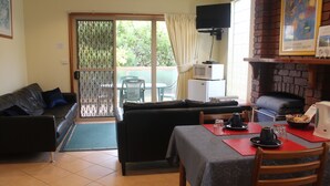 A cozy living area with a sofa, a dining table set with plates and cups, and a kitchen area with a microwave. - Angela's Beach Stays (Apollo Bay)