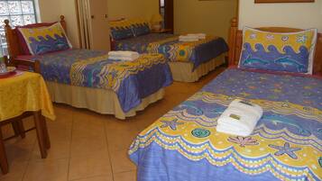 Quarto de hotel com duas camas, cada uma com colcha colorida com desenhos de criaturas marinhas. Há uma pequena mesa com toalha de mesa amarela e uma cadeira.