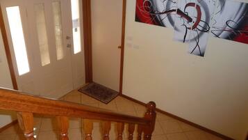 A staircase with wooden balusters and a handrail, leading to a landing with a doormat and a door with frosted glass panels.