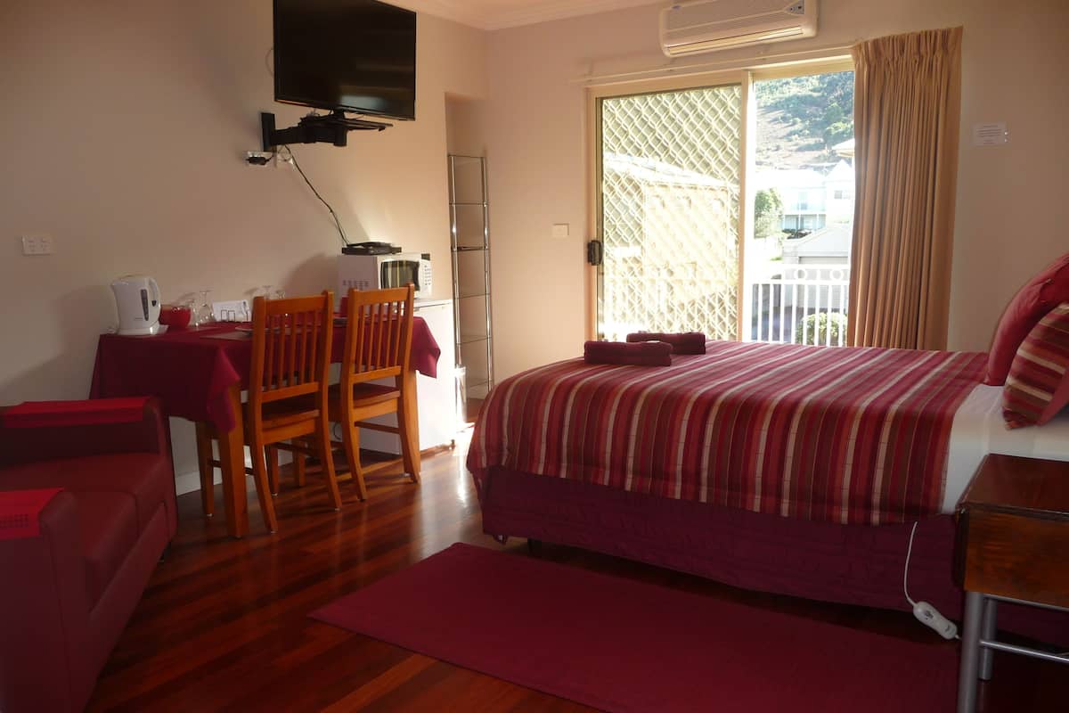 Quarto de hotel com uma cama, uma escrivaninha com cadeira, televisão na parede e varanda com vista para o exterior.