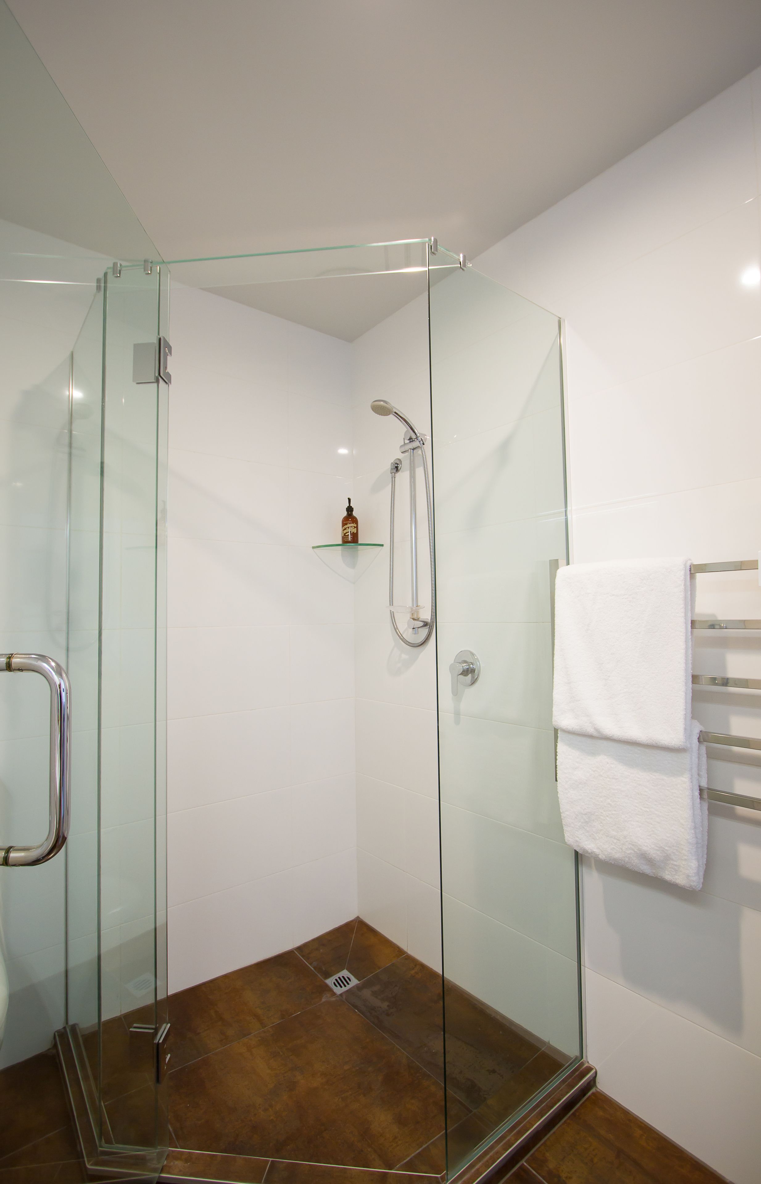 A glass-enclosed shower area with a white towel rack and a small shelf.