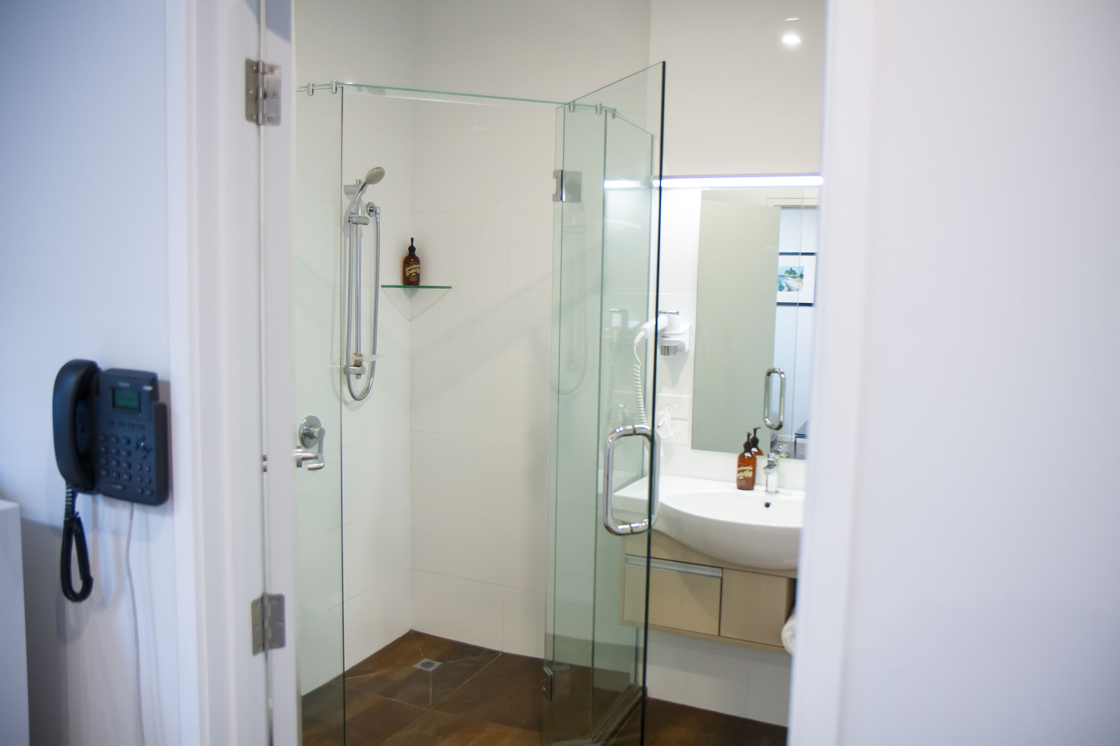 A modern bathroom with a glass shower enclosure, a built-in sink, and a telephone mounted on the wall.