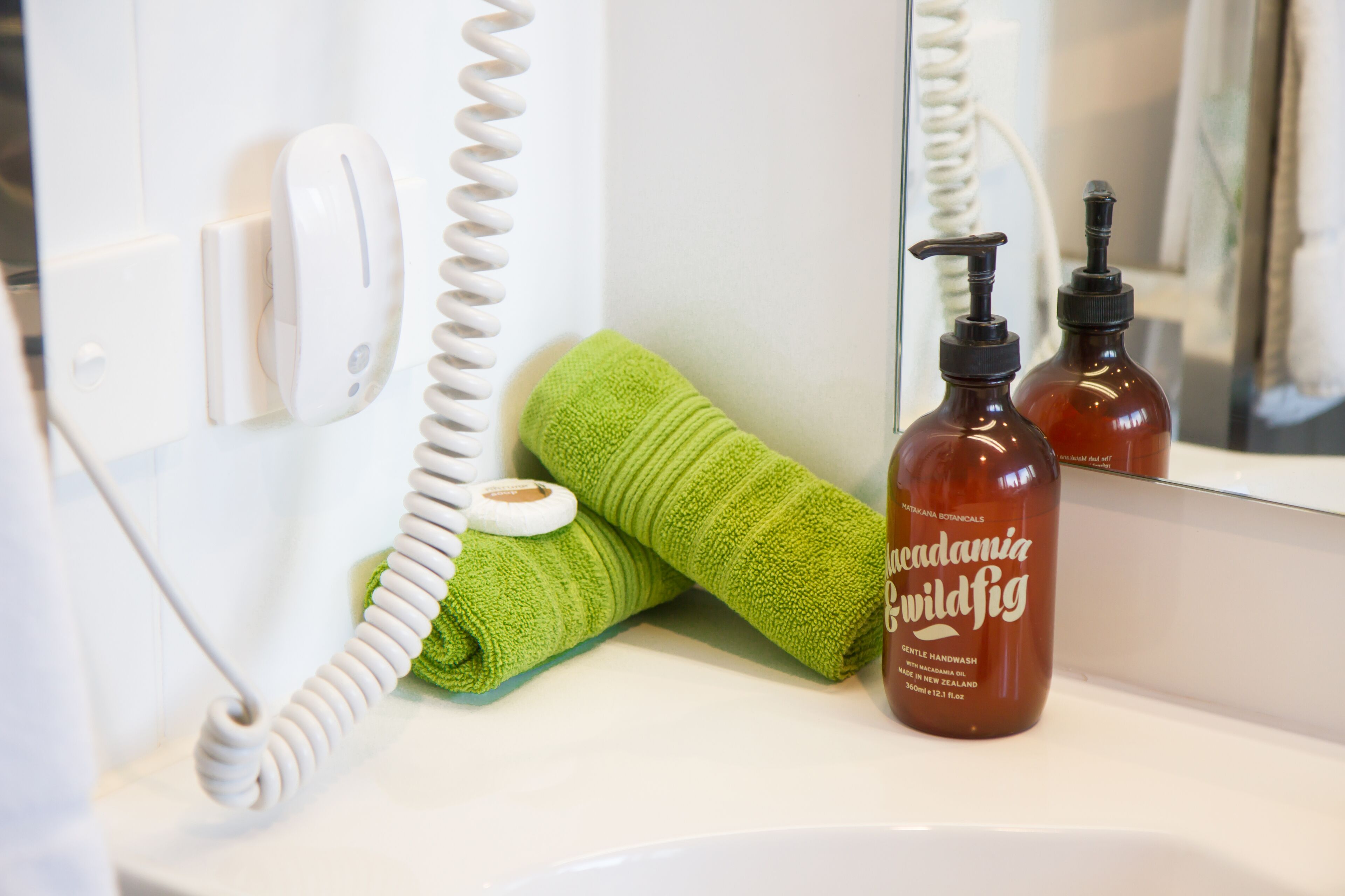 A bathroom with a white telephone, a green towel, and two bottles of Wild Fig handwash.