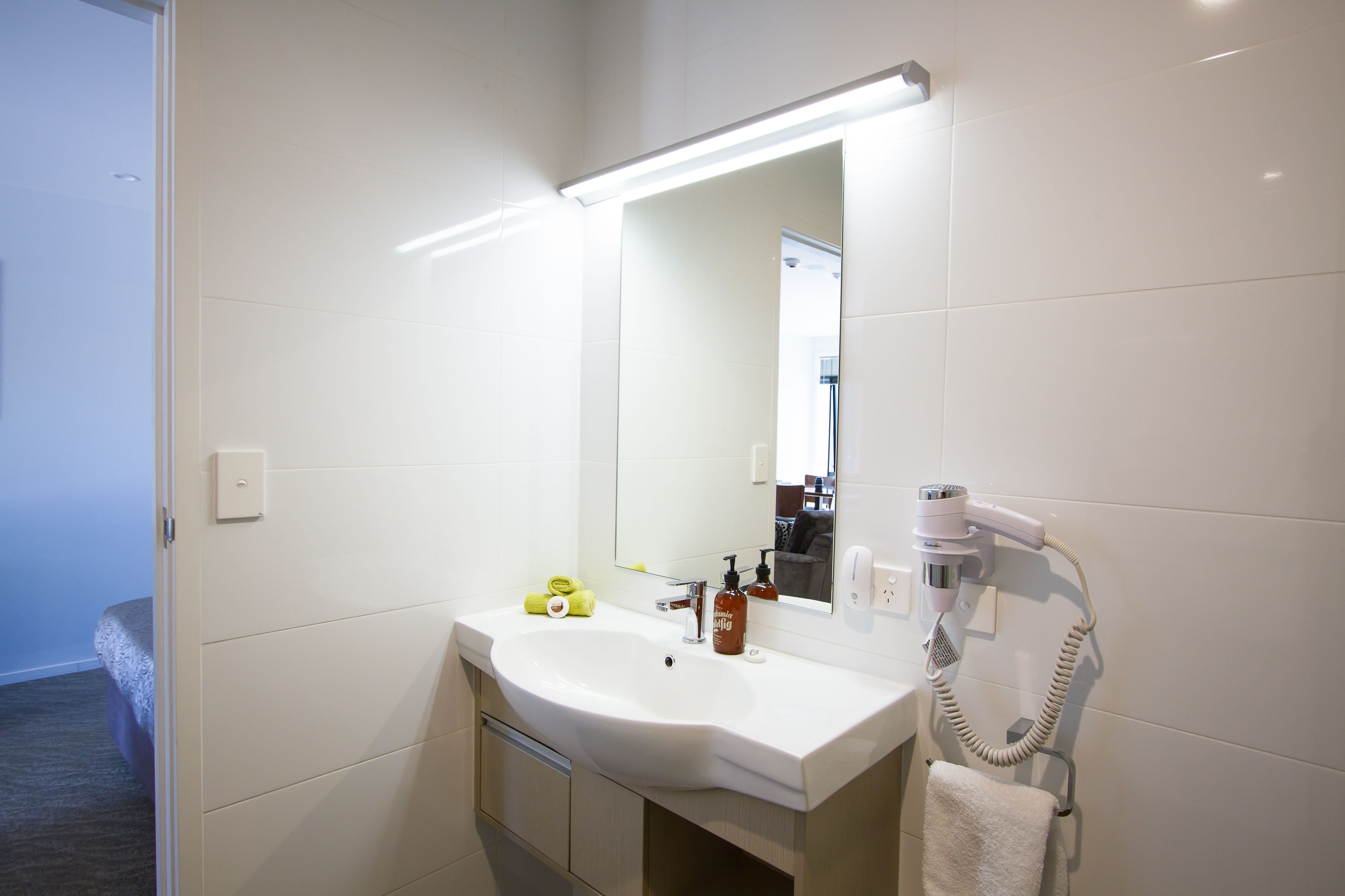 Un baño moderno con un lavamanos blanco, un espejo y un secador de pelo montado en la pared.