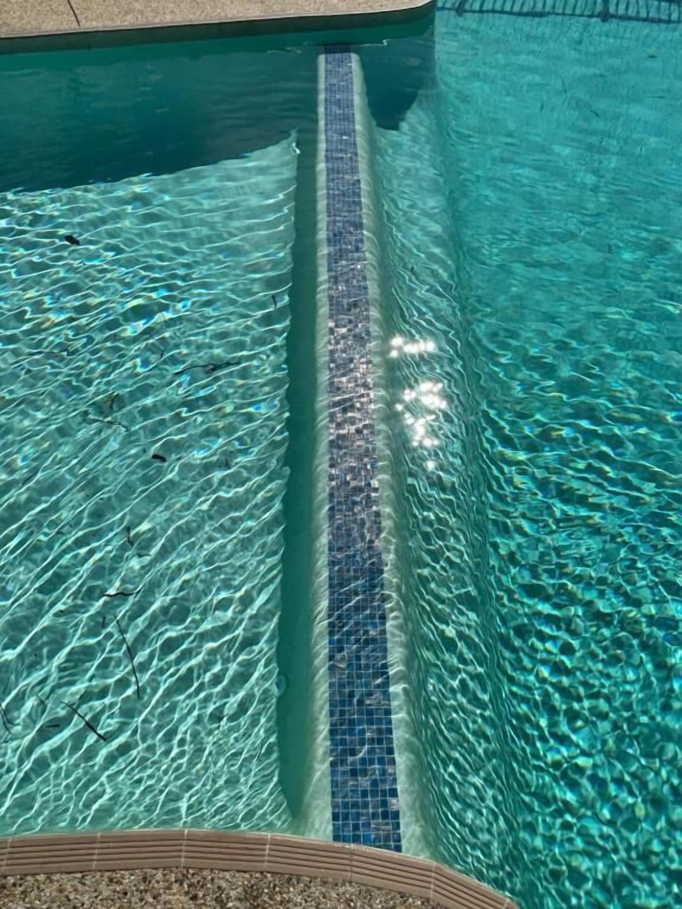 Une piscine aux eaux claires, bordée de carreaux et dont le fond est recouvert de galets.