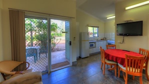 A compact kitchen with a dining area, a TV mounted on the wall, and a sliding glass door leading to an outdoor patio. - Batchelor Holiday Park (Batchelor)