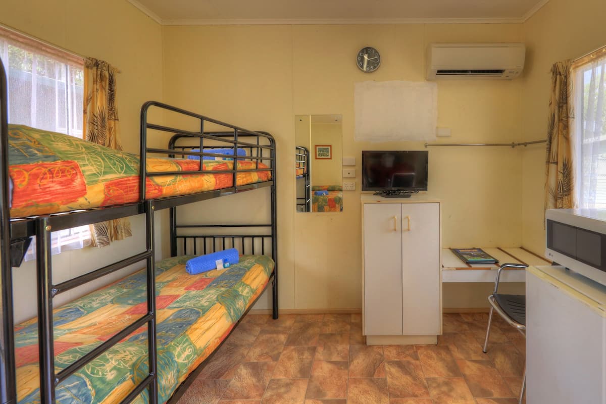 A dormitory room with bunk beds, a desk with a TV, a microwave, and a cabinet.