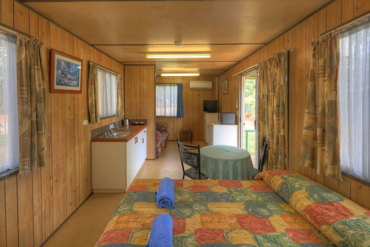 A compact room with a bed, a small kitchenette, a dining area, and a TV.