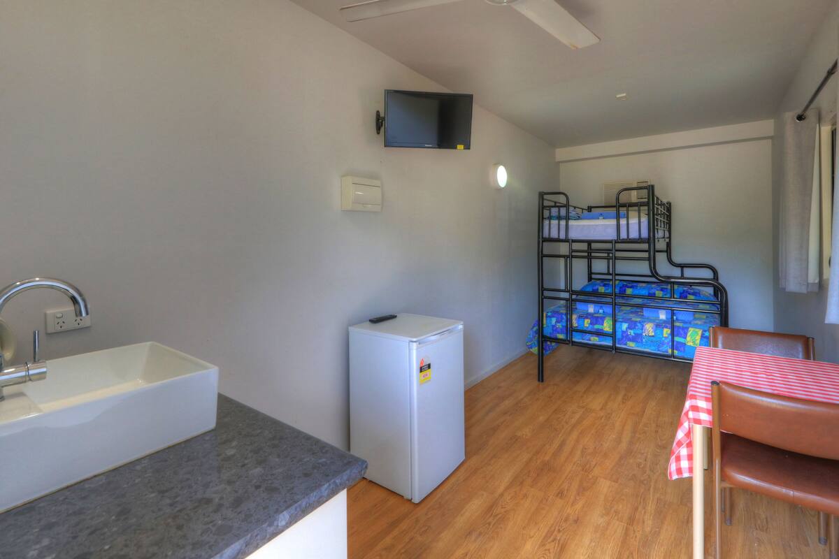 A compact kitchenette with a sink, a small refrigerator, and a bunk bed with a table and chair.