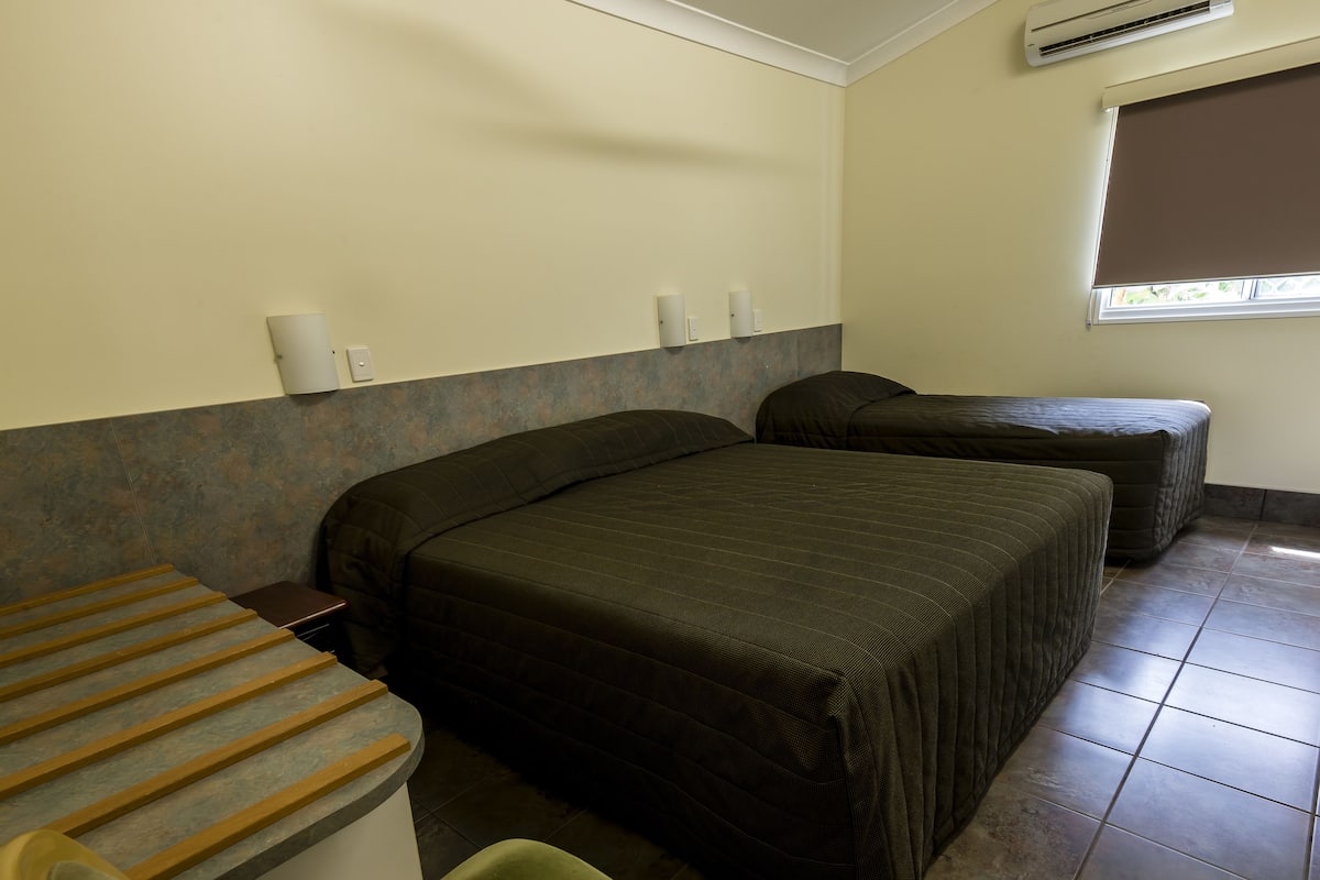 A hotel room with two beds, a small desk, and a window with a blind.