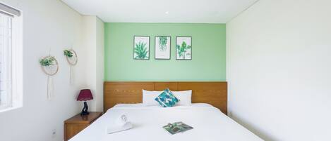 Una cama bien hecha con sábanas blancas, cabecera de madera y un ventilador de techo. Hay tres láminas enmarcadas con motivos botánicos en la pared sobre la cama.