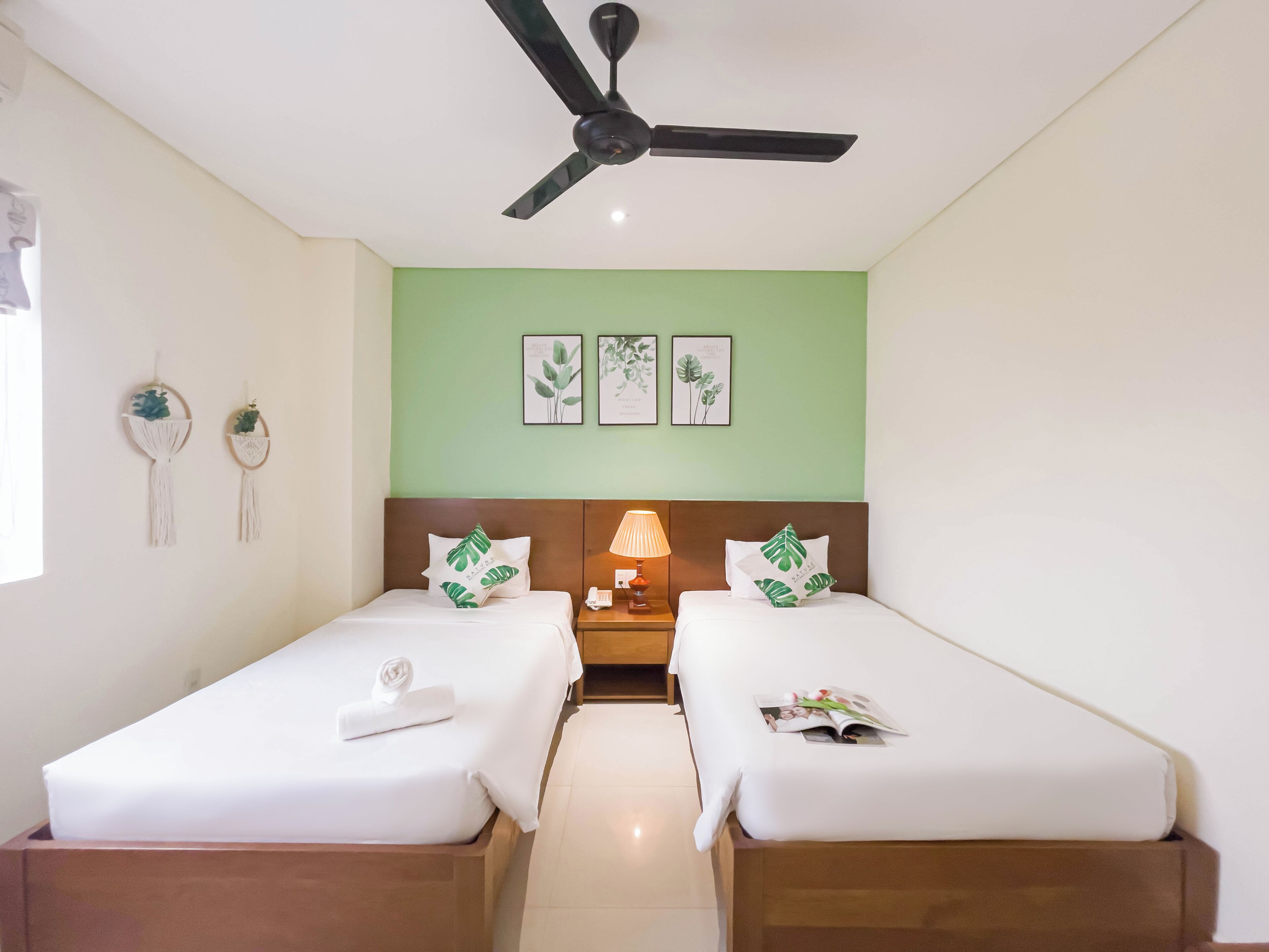 A hotel room with two beds, a ceiling fan, a nightstand with a lamp, and wall art.
