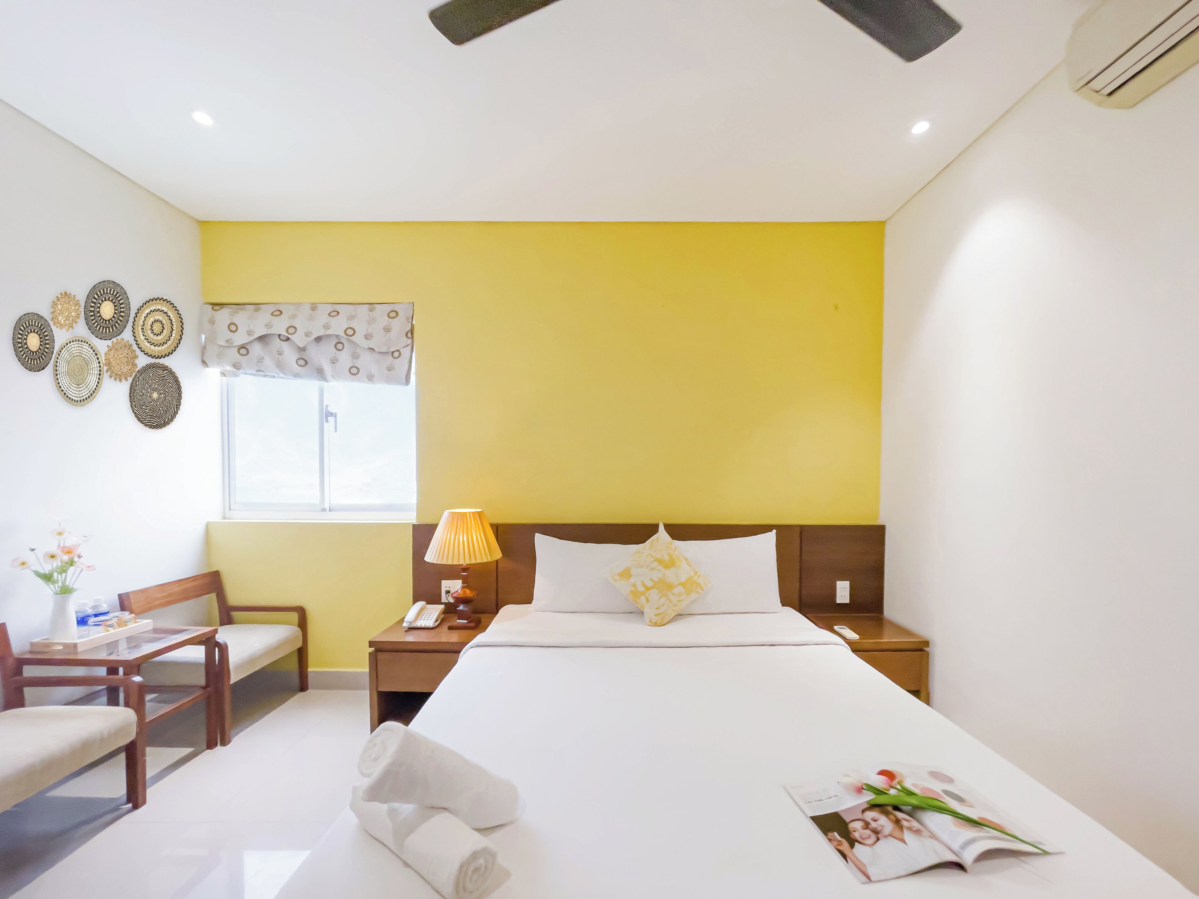 Ein Hotelzimmer mit Bett, Nachttisch, Lampe, Sessel und Wandbild.
