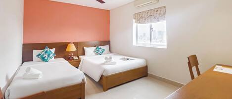 A hotel room with two beds, a ceiling fan, an air conditioning unit, a window with a view of the city, and a wooden table.