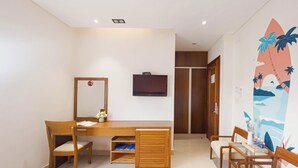 Une chambre d’hôtel avec un bureau en bois, des chaises, une télévision, une armoire et une fresque murale sur le thème de la plage.