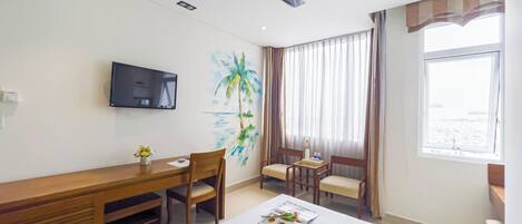 Una habitación de hotel con cama, escritorio, silla, televisor y ventana con cortinas.