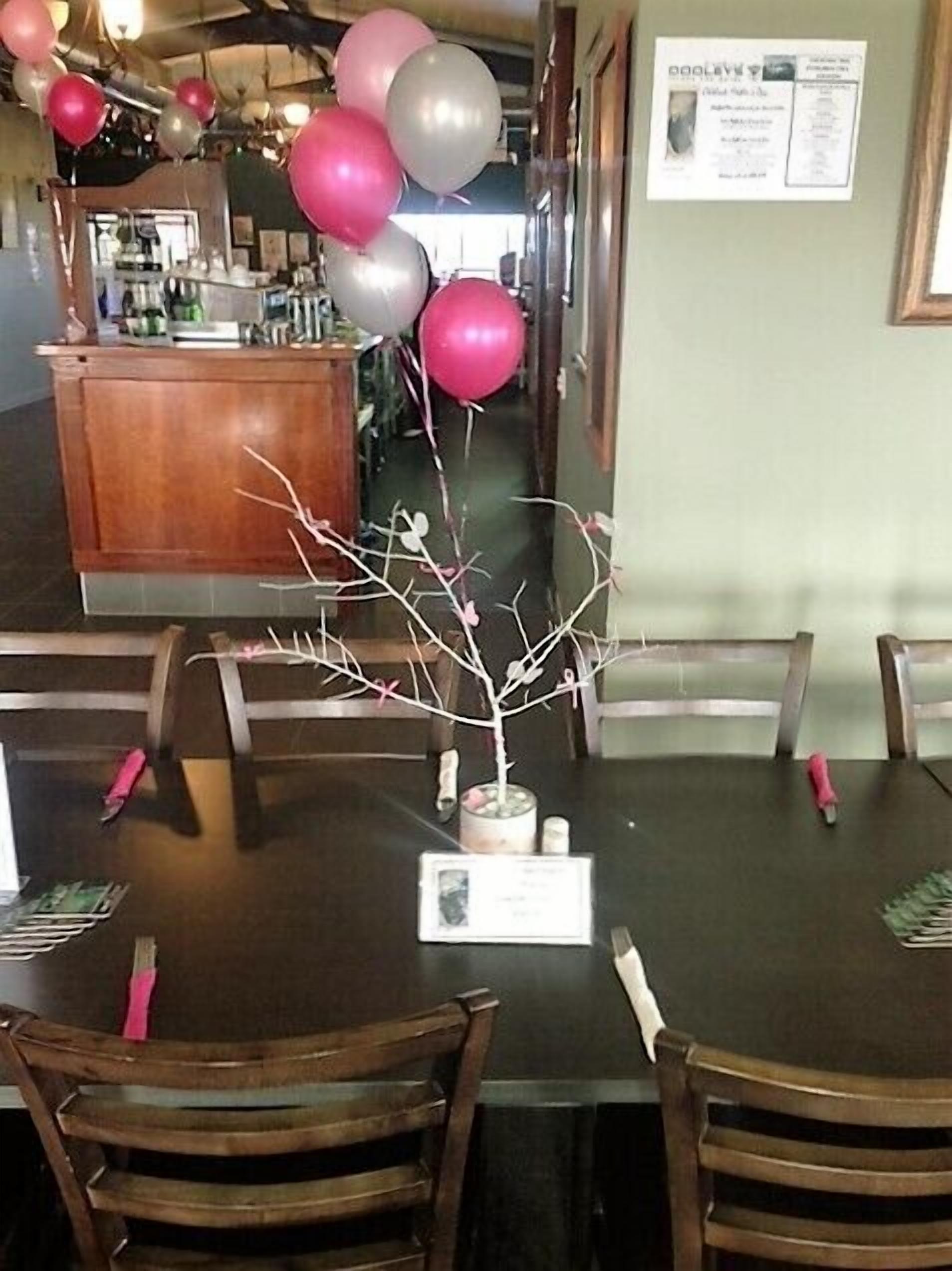 Un interior de restaurante con mesas y sillas de madera, un mostrador de recepción y globos.