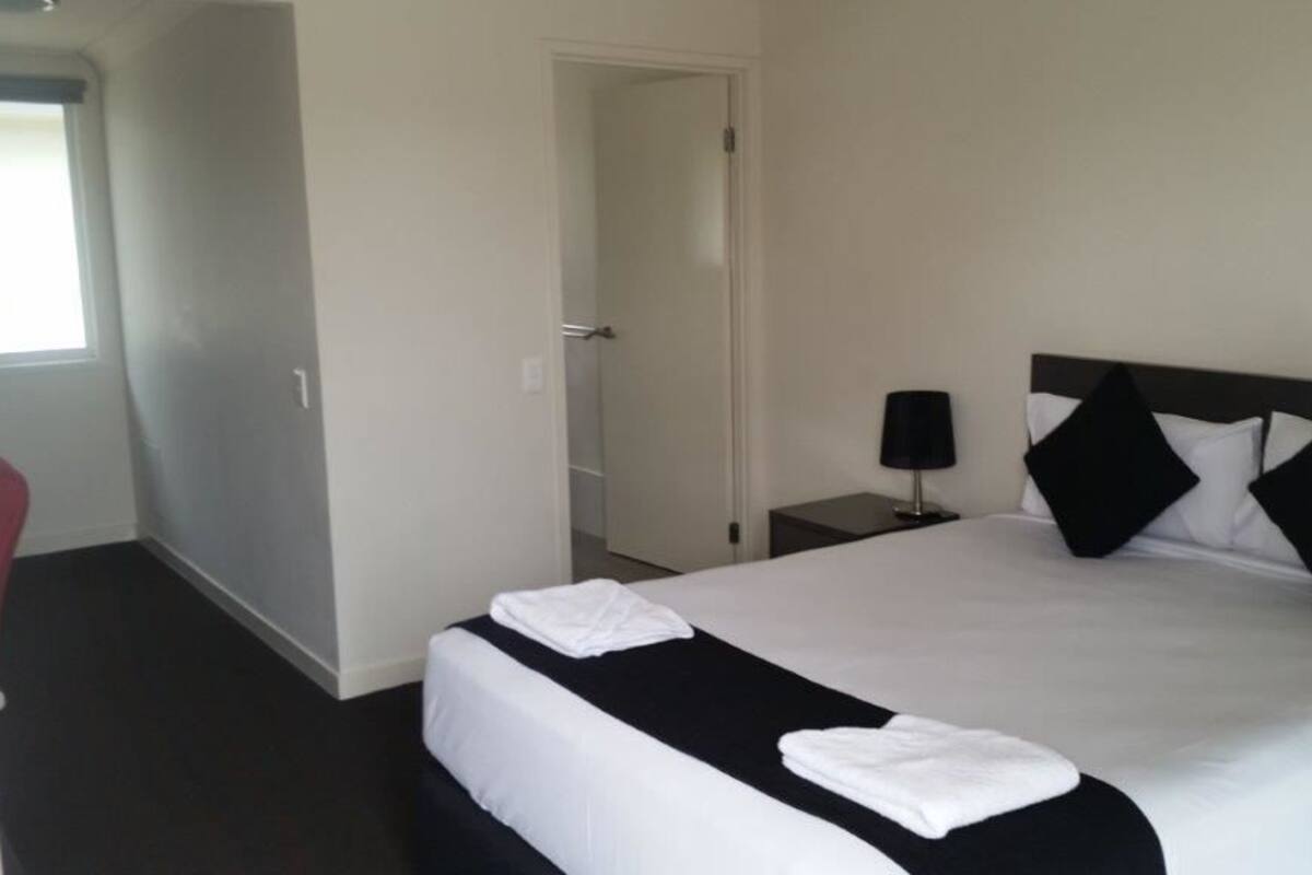 Une chambre d’hôtel avec un grand lit, une table de chevet avec une lampe et une porte donnant sur une autre pièce.