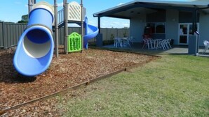 Ein Spielplatz mit Rutsche, Klettergerüst und einer überdachten Terrasse mit Sitzgelegenheiten.