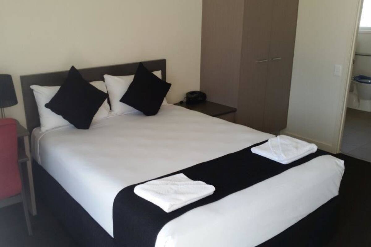 Une chambre d’hôtel avec un lit, une table de chevet, une armoire rouge et une garde-robe.