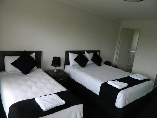 Una habitación de hotel con dos camas, cada una con ropa de cama blanco y negro, una mesita de noche con lámpara y una puerta que da a otra habitación.