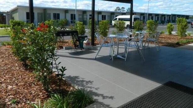 Eine Außenpatio-Terrasse mit Metalltischen und -stühlen, umgeben von Pflanzen und einem überdachten Sitzbereich.
