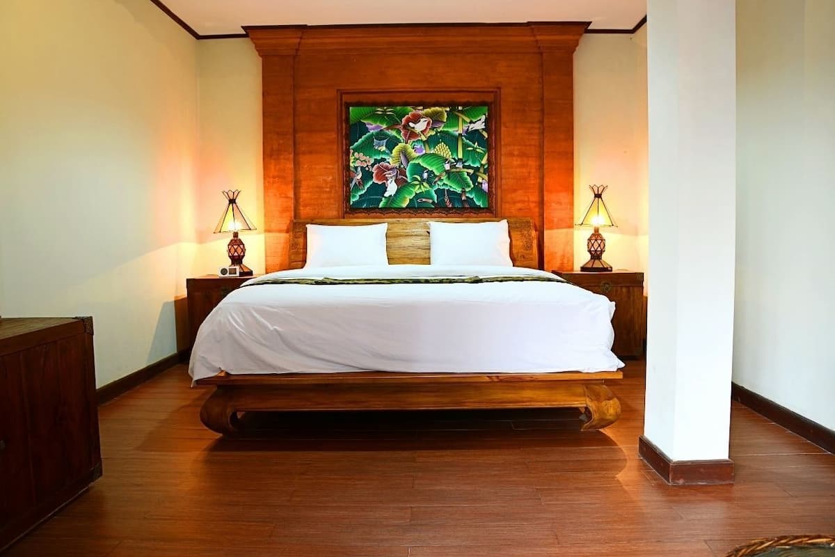 A large bed with a wooden headboard, two bedside lamps, and a large floral artwork above the bed.