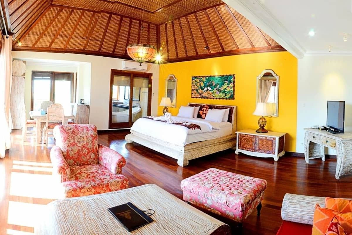 A spacious room with a large bed, a dining area, and a TV.