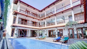 Un hotel de varios pisos con piscina en un patio central, balcones y zonas de estar al aire libre.
