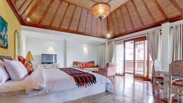 Un dormitorio amplio con una cama grande, televisión y un balcón con muebles de mimbre.