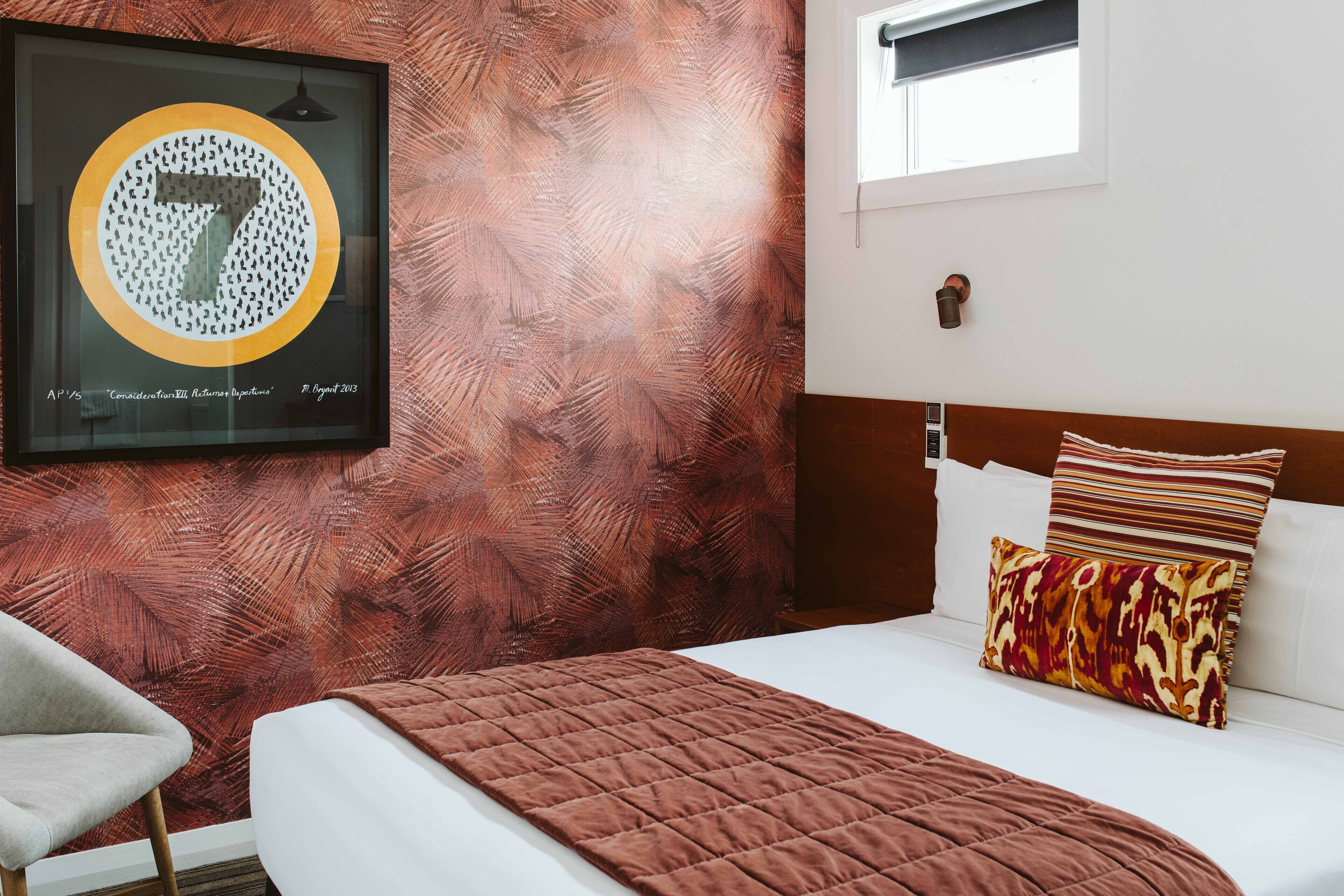 Una camera d'albergo con un letto, una poltrona, un'opera d'arte incorniciata appesa al muro e una finestra.